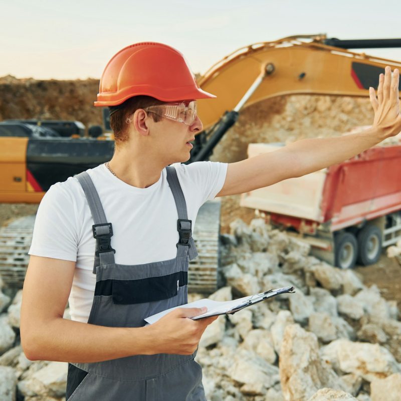 Management of project. Worker in professional uniform is on the borrow pit at daytime